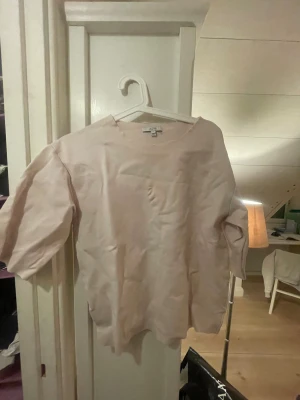 Ljusrosa blus från Dagmar, strl 36 - Säljer en stilren ljusrosa blus från Dagmar i storlek 36. Tröjan har en rak passform, rund halsringning och trekvartsärmar. Materialet är ganska tjockt. Observera att tröjan har en defekt på framsidan, men perfekt för någon som vill fixa den med coolt tryck.