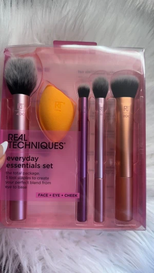 Real Techniques Everyday Essentials Set - Säljer ett Real Techniques Everyday Essentials Set med fem verktyg: fyra sminkborstar i metallic rosa, lila och koppar samt en orange beautyblender. Borstarna är mjuka och täta, perfekta för foundation, rouge, ögonskugga och setting. Cruelty-free och veganska.
