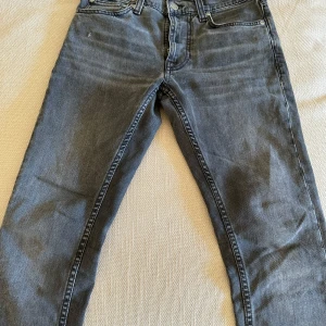 Svarta jeans från Nudie Jeans, W27 L28 - Säljer ett par svarta jeans från Nudie Jeans med klassisk femficksdesign och svarta broderade detaljer på bakfickorna. Jeansen har normal passform och raka ben, tillverkade i mjuk bomullsdenim. Perfekta för dig som gillar stilrena och tidlösa jeans. Anledningen till försäljningen är för att dom helt enkelt inte passar längre. Modell lean Dean! W27 L28