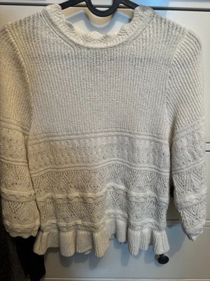 Vit stickad tröja från H&M - Supersöt vit stickad tröja från H&M DIVIDED i storlek S. Tröjan har långärmade ärmar, volangkant nedtill och ett snyggt mönster med olika stickade strukturer. Perfekt för dig som gillar detaljer och vill ha en mysig look.