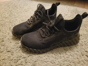 Svarta Adidas sneakers med grov sula - Säljer ett par svarta Adidas sneakers med chunky, räfflad sula och stickad ovandel. Skorna har snörning och diskret Adidas-logga på sidan. Perfekta för dig som gillar sportig stil och vill ha bekväma skor med cool design. Använda 3 ggr och i nyskick, behöver dammas av bara!