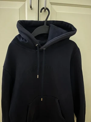 Mörkblå hoodie från J.Lindeberg - Snygg mörkblå hoodie från J.Lindeberg. Den är i stormek L på barnstorlek, som motsvarar XS/S på vuxenstorlek. Den är i fint skick och passar bäst om du är mellan 165-175cm. Ny pris är 1100kr.