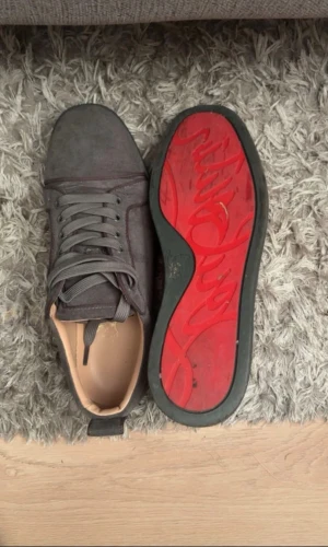 Grå mocka sneakers med röd sula - Snygga grå sneakers i mocka med platt sula och rund tå. Skorna har snörning och en unik röd undersida med grafiskt mönster. Insidan är beige och de har diskreta sömmar som ger en stilren look. Perfekta för dig som gillar detaljer och vill sticka ut. Vid minsta lila fundering så hör av er.