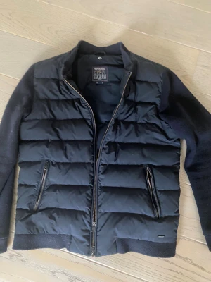 Woolrich - Snygg svart pufferjacka från Woolrich med quiltad front och mjuka stickade ärmar. Jackan har två dragkedjeförsedda fickor och hel dragkedja framtill. Perfekt för dig som gillar stilren och sportig look med en modern touch.