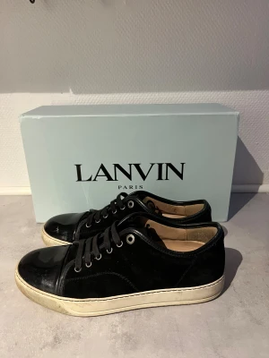 Svarta sneakers från Lanvin Paris - Svarta sneakers från Lanvin Paris med snygg kontrast mellan mocka och blankt skinn på tån. Klassisk rund tå, snörning och vit platt sula. Insidan är beige och skorna har en stilren, lyxig vibe som passar till jeans eller dressade outfits. köpta på care of Carl, tveka inte på att höra av er! 