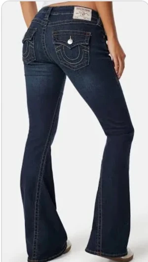 Mörkblå bootcut jeans från True Religion - Snygga mörkblå jeans från True Religion med bootcut passform och klassiska kontrastsömmar. Baktill finns stora fickor med dekorativa sömmar och knappstängning. Jeansen har låg midja och är tillverkade i stretchigt denim för skön passform.