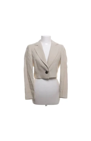 Beige croppad kavaj från Zara - Snygg beige croppad kavaj från Zara med klassisk krage och en knapp framtill. Jackan har lång ärm och är tillverkad i ett lätt material med slät yta. Perfekt för dig som vill ha en trendig och stilren look.