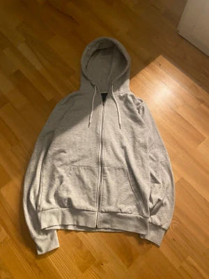 Zip hoodie - Grå hoodie från 157 i storlek S. Tröjan har huva med snörning, praktiska fickor framtill och hel dragkedja. Tillverkad i mjuk bomullsmix som känns skön mot huden. Perfekt för chill dagar och när du vill ha en enkel, clean look. Passformen är baggy och insidan är skön, mjuk och känns som en filt. Den har aldrig varit använd eftersom den var för liten när jag provade på den och sen dess har den legat runt.