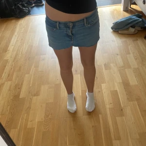 Ljusblå jeanskjol från Levi's - Säljer en ljusblå jeanskjol från Levi's med rå kant nertill och klassiska femficksdetaljer. Modellen är kort , perfekt till sneakers eller boots. Levi's-logga på bakfickan och knappstängning framtill. Superenkel att styla till olika looks.