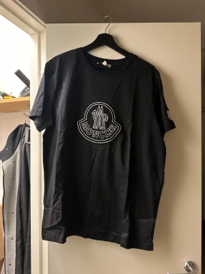 Svart Moncler t-shirt med logga - Säljer en svart t-shirt från Moncler med stor vit broderad logga på bröstet och en mindre logga på ärmen.