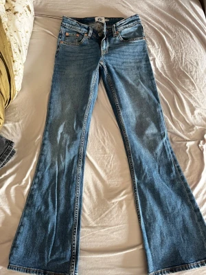 Blå bootcut jeans från 157 XXS - Bootcut jeans från 157 i ljusblå tvätt med låg midja. Klassisk femficksmodell med orangea sömmar och knappstängning fram. Jeansen är tillverkade i jeansmaterial och har en snygg bootcut-passform som ger en schysst siluett.