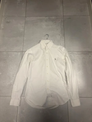 Vit slim fit skjorta från Ralph Lauren - Vit skjorta från Ralph Lauren i slim fit-modell med klassisk krage och knappar framtill. Skjortan har lång ärm och det ikoniska broderade logotypen på bröstet. Storlek Small. Fint skick. Pris diskuteras vid snabb affär.