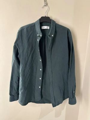 Mörkgrön skjorta från Samsoe Samsoe - Snygg mörkgrön skjorta från Samsoe Samsoe med klassisk krage och vita knappar. Skjortan är långärmad och har en stilren, enkel design som funkar till många olika looks. Tillverkad i mjuk bomull för skön känsla hela dagen.