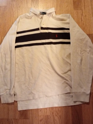 Vit långärmad polotopp från Polo Ralph Lauren - Säljer en vit långärmad polotopp från Polo Ralph Lauren med svarta horisontella ränder och röd broderad logga på bröstet. Toppen har krage och knappar vid halsen, tillverkad i bomull med en klassisk loose passform pris kan självklart diskuteras om du har några frågor så är det bara att skriva ✅🙌