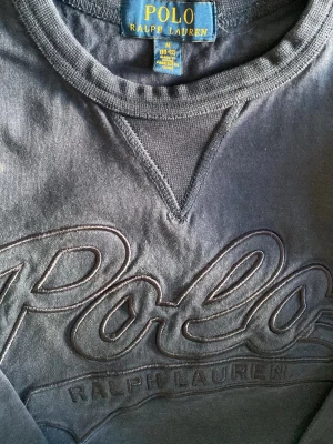 Mörkblå sweatshirt från Polo Ralph Lauren - Snygg mörkblå sweatshirt från Polo Ralph Lauren med stort broderat logotyp på bröstet. Tröjan har rund hals, ribbade muddar och långa ärmar. Perfekt för dig som gillar klassisk streetstil och vill ha något bekvämt och stilrent.