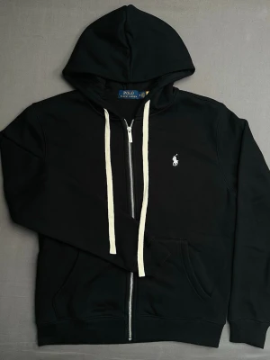Svart hoodie från polo Ralph lauren  - Snygg svart hoodie med dragkedja från polo Ralph lauren med vit broderad logga på framsidan. Bra skick endast testad på en gång