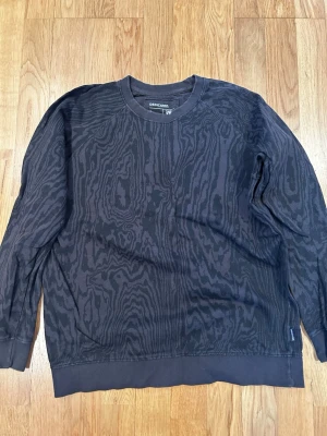 Svart mönstrad sweatshirt från Dedicated - Cool svart sweatshirt från Dedicated i 100% ekologisk bomull. Tröjan har ett unikt mönster som påminner om träådring och klassisk rund hals. Långa ärmar och ribbade muddar vid ärmslut och nederkant ger en skön passform.