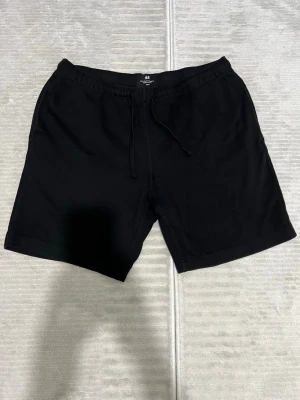 Svarta shorts från H&M med snörning - Svarta midwaist shorts från H&M i regular fit. De har snörning i midjan och är tillverkade i mjukt bomullstyg. Perfekta för chill dagar eller när du vill ha något enkelt och bekvämt.