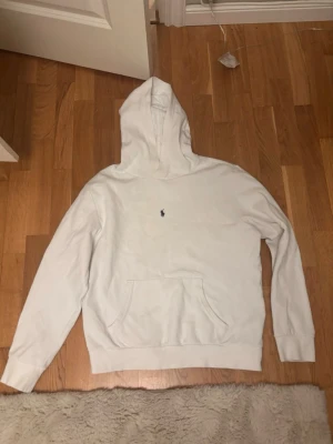Vit hoodie från Ralph Lauren - Säljer en stilren vit hoodie från Polo Ralph Lauren med den klassiska broderade loggan på bröstet. Den är i toppen skick förutom den pyttelilla defekten ni kan se på sista bilden som knappt märks. Storlek 18/20 barnstorlek vilket motsvarar en S eller eventuellt en mindre M. Vid några frågor eller funderingar är det bara att höra av sig.