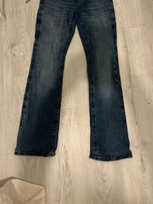 Blå bootcut jeans från Gina Tricot - Snygga blå jeans från Gina Tricot i bootcut-modell med cool paljettdekor på bakfickan. Jeansen har klassisk femficksdesign och är gjorda i slitstarkt denimtyg. Perfekt för dig som vill ha en unik detalj på dina jeans.