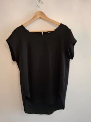 Svart blus från ONLY med dragkedja - Säljer en stilren svart blus från ONLY i storlek 40. Blusen har korta ärmar, rund halsringning och en snygg silverfärgad dragkedja i ryggen. Materialet är slätt och lätt, perfekt för dig som gillar enkel och clean stil.