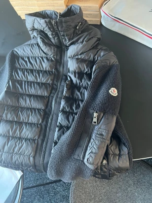 Svart Moncler cardigan jacka M - Svart cardigan jacka från Moncler med stickade ärmar och detaljerad ficka med dragkedja på ena ärmen. Köpte den i monclers egna butik så jag alla og saker. Perfekt för dig som vill ha en snygg cardigan.