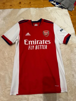 Arsenal tröja - Säljer en officiell Arsenal matchtröja från Adidas i storlek M. Tröjan är röd med vita ärmar och mörkblå detaljer vid krage och ärmslut.