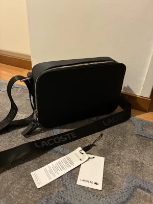 Svart axelväska från Lacoste - Den är oanvänd,De kommer med taggar 