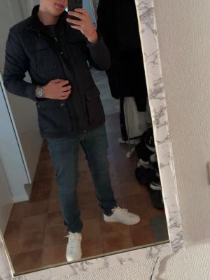 Mörkblå quiltad jacka - Säljer en mörkblå quiltad jacka med dragkedja och knappar. Jackan har flera fickor med knappdetaljer och en hög krage. Perfekt för kyligare dagar.S i storlek men passar även M! 9/10 skick knappast använd inga defekter alls