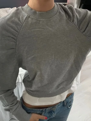 Grå sweatshirt från H&M, XS - Säljer en grå sweatshirt från H&M i storlek XS. Tröjan har rund hals, ribbade muddar och snygga rynkade detaljer vid axlarna. Modellen är croppad och har en loose passform som ger en chill vibe. Perfekt att matcha med jeans eller leggings.