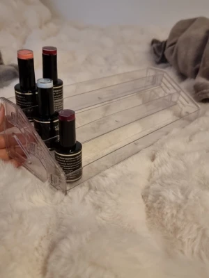 Genomskinlig sminkförvaring i plast - Säljer en genomskinlig sminkförvaring i hård plast med tre trappsteg, perfekt för att organisera smink som läppstift, läppglans eller nagellack. Enkel och stilren design som passar på sminkbordet eller i badrummet.