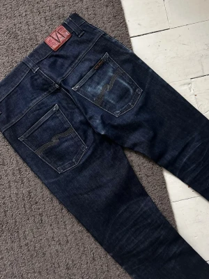 Mörkblåa Nudie Dry Thin Finn Jeans - Riktigt stilrena Nudie Dry Jeans i Thinn Finn modell. | W30 L32 | Riktigt fint skick, liten slitning vid cuffsen som ej syns. Längd: 107cm, Midja: 37-41cm (Stretch). | Väldigt tydliga fades! | Pris ej hugget i sten, skriv vid minsta fundering.