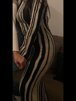 Randig långklänning från NA-KD - Säljer en långärmad långklänning från NA-KD med svart och beige oregelbundet randigt mönster. Obs.. släppt sömn vid taggen, i övrigt i gott skick!