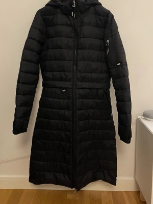 Svart lång ridkappa från CRW - Superfin svart ridkappa från CRW! Används flertal ggr men fortfarande super fint skick utan defekter! Flera fickor med dragkedjor. Kan dras åt i midjan. Avtagbar huva. Har knappar som man kan knäppa upp så den går att rida med! Kan även skicka flera bilder privat💞 