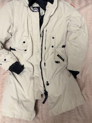 Beige parkajacka från Canada Goose M - Säljer min  vinterjacka från Canada Goose  i storlek M. Mycket varm och slitstark jacka, perfekt för kalla vinterdagar. Jackan är använd men i gott skick.  Äkta produkt med originalmärken.  Skick: Bra Storlek: M Färg: Ljus beige Märke: Canada Goose Nypris: ca 10 000–13 000 kr 