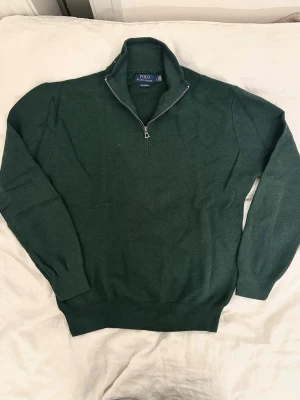 Grön half zip tröja Polo Ralph Lauren - Mörkgrön långärmad tröja från Polo Ralph Lauren i mjuk pima bomull. Tröjan har en klassisk half zip-dragkedja och ribbade muddar vid ärmslut och nederkant. Passar M/L.