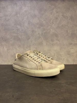 Axel Arigato Clean 90 - Säljer ett par Axel Arigato Clean 90 stilrena ljusgrå sneakers i mocka med vita detaljer och platt sula. Skorna har klassisk snörning och minimalistisk design, perfekt till jeans eller chinos. Diskret logga på sidan och vit häl i skinn för extra kontrast. I fint skick utöver vanligt slitage från användning!