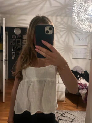 Vit linnetopp med knyt i ryggen - Supersöt vit linnetopp från Nelly med tunna axelband och volangig, luftig passform. Toppen har band som man knyter till en rosett bak i ryggen. Enkel att styla med jeans eller kjol. Aldrig använd och därför prislapp kvar.