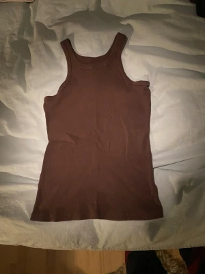 Brun ribbad linnetopp från 157 - Säljer en brun ribbad linnetopp från 157 i storlek XS. Toppen är ärmlös med breda axelband och har en enkel, stilren design. Tillverkad i 100% bomull vilket gör den mjuk och skön att bära. Perfekt att matcha med jeans eller kjol.