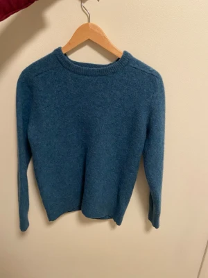Blå ulltröja från A Day's March  - Mysig blå stickad tröja från A Day's March i 100% ull. Det står att den är i strl M men jag skulle säga XS. Kostar nypris 1500kr men jag säljer för 500kr eftersom den har råkat tvättats lite för varmt och därför krympt något i strl. 