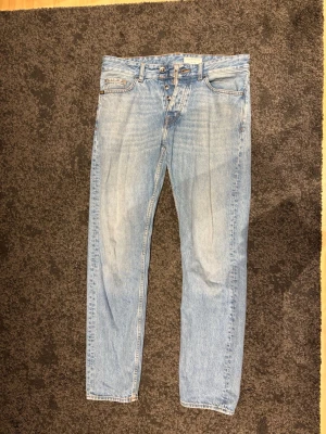 Ljusblå jeans från Tiger of Sweden - Säljer ett par ljusblå jeans från Tiger of Sweden med klassisk femficksdesign och knappgylf. Jeansen har raka ben och snygga kontrastsömmar. Perfekta för dig som gillar en tidlös och clean look. Modellen är enkel att styla med allt.