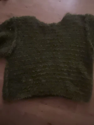 Grön fluffig stickad tröja - Mysig grön stickad tröja med fluffig känsla. Tröjan har en loose passform och är perfekt för kyliga dagar. Den har kortare ärmar och en enkel design som gör den lätt att matcha med olika outfits.