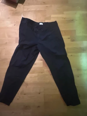 Svarta chinos med tapered passform - Säljer ett par svarta chinos med tapered ben och klassisk design. Byxorna har normal midja och är tillverkade i ett mjukt bomullsmaterial som känns skönt mot huden. Perfekta för dig som gillar en stilren och enkel look.