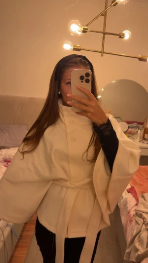 Poncho Jacka Gina tricot  - Säljer en stilren poncho/kappa med knappar framtill och bälte i midjan, från Gina Tricot, använd fåtal gånger, inga defekter alls, skulle säga att den är som ny! Jackan har vida ärmar och en elegant, enkel design som ger en clean look. Perfekt för dig som gillar minimalistisk stil och vill ha något som sticker ut på ett classy sätt. 