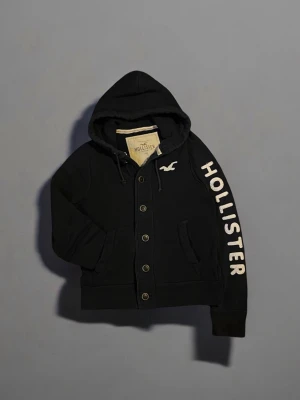 Hollister hoodie – Svart, L,stilren & väldigt sällsynt  - Snygg och bekväm hoodie från Hollister i storlek XL men passar mer som L (se mått)  Svart färg med vit logga (seagull) på bröstet och “HOLLISTER” tryckt längs ärmen.   Knappar framtill, två fickor och dragsko i huvan. Perfekt för dig som gillar avslappnad stil med premiumkänsla.  ✅ Mjukt material ✅ Stilren design ✅ Passar både vardag och chill ✅ Bra skick – inga fläckar eller hål  || bred~ 53 || längd~ 61   Står Xl men passar mer som en L   #hollister  #hoodie #svarttröja #herrkläder #streetwear