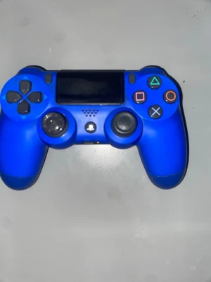 PlayStation DualShock 4 Wireless Controller - Blå PlayStation DualShock 4 trådlös handkontroll i gott skick. Alla knappar och styrspakar syns tydligt, och inga större repor eller skador är synliga. Perfekt för PlayStation 4-spelare som vill ha en extra eller ersättningskontroll. Lite sönder vänster spak.