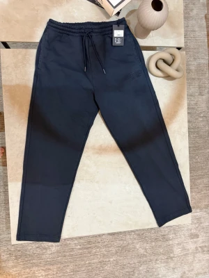 Mörkblå mjukisbyxor från Missoni Sport - Snygga mörkblå mjukisbyxor från Missoni Sport med broderad logga på benet. Byxorna har elastisk midja med snörning och raka ben. Tillverkade i mjuk bomull för maximal komfort. Perfekta för chill dagar eller när du vill ha en clean look.size S but fits size M because its baggy. New price is 400-520 dollars