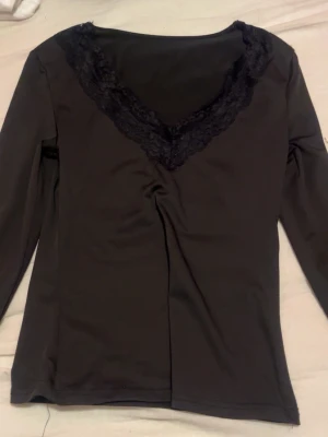 Svart långärmad topp med spets - Svart tunn långärmad topp med djup v-ringning och dekorativ spets runt halsen. Toppens material känns mjukt och stretchigt, perfekt för en stilren look. Passar dig som gillar enkla men snygga detaljer. Knappt använd, Xs 😘