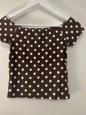 Brun prickig offshoulder topp M - Snygg brun offshoulder topp med vita prickar. Toppens färg kallas Chocolate Martini/Star White och den har korta ärmar. Perfekt för dig som gillar trendiga mönster och en lite lekfull stil.