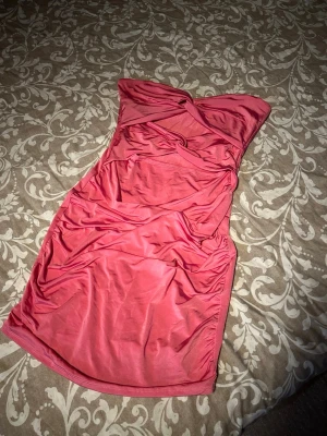 Rosa offshoulder kortklänning - Säljer en snygg rosa kortklänning med offshoulder-design och draperade detaljer framtill. Klänningen har twistad effekt vid bysten och är tillverkad i ett mjukt, stretchigt material som sitter tajt och markerar figuren. Perfekt för dig som vill sticka ut med en cool look. Aldrig använd.